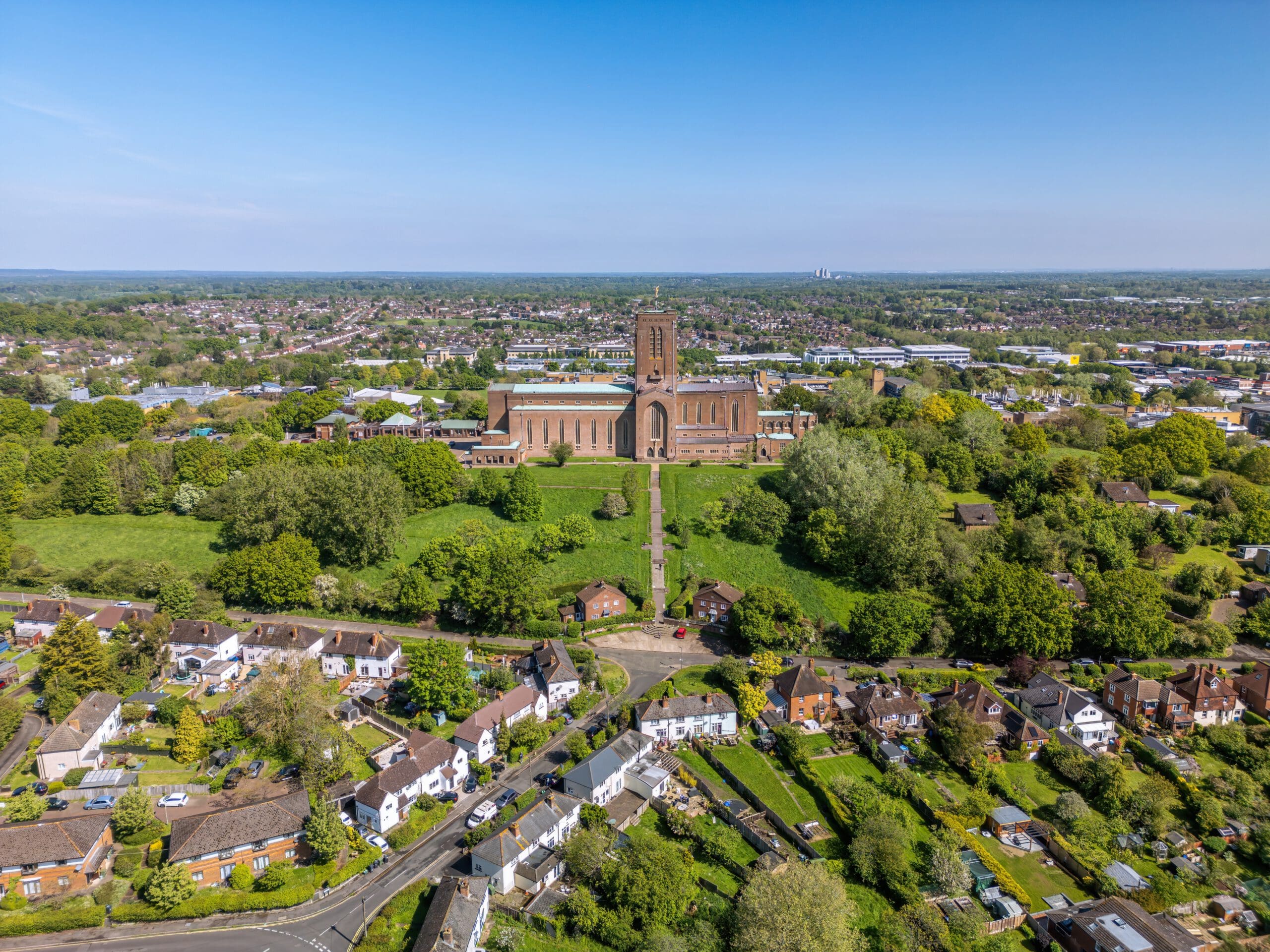 Aerial view of a large cathedral surrounded by greenery, with residential houses in the foreground and a sprawling town beyond—an ideal setting for a property maintenance company offering fascia and guttering installation under a clear blue sky.